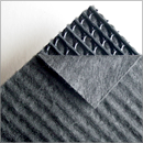 A close-up image of a dark gray textured mat with a corner lifted, revealing a layered structure and grid pattern underneath.